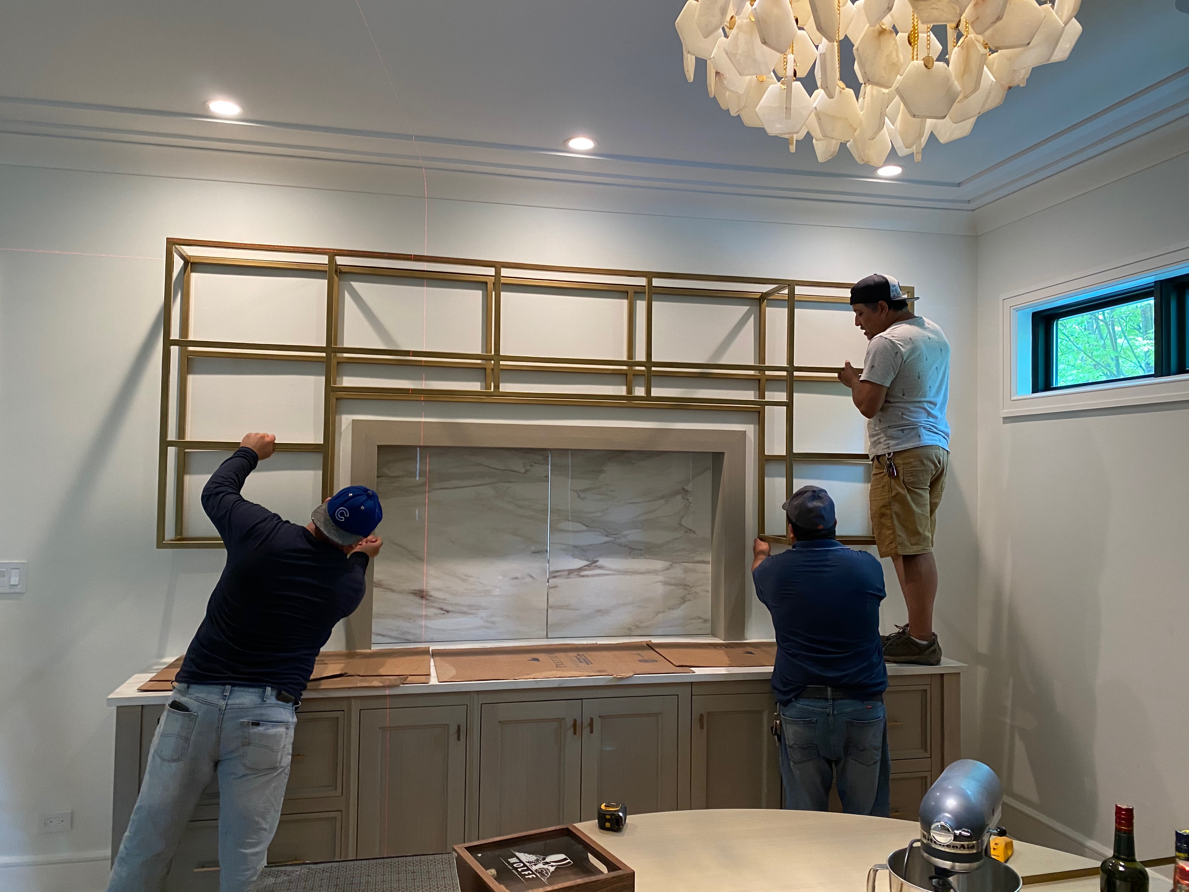 Crew leveling and installing the custom gold-finished steel shelving over the bar