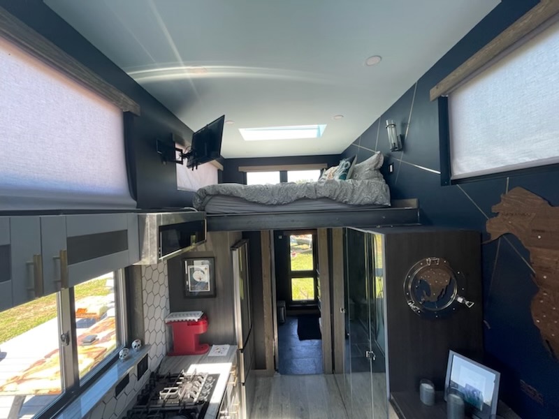 Daylit interior view of the Mini House with lofted sleeping above the compact kitchen