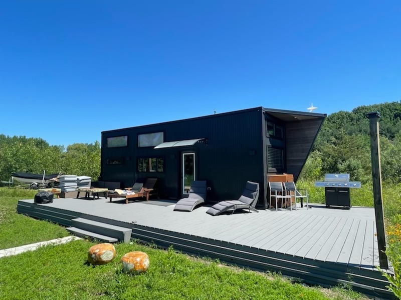Finished exterior deck with lounge seating beside the compact black-clad home