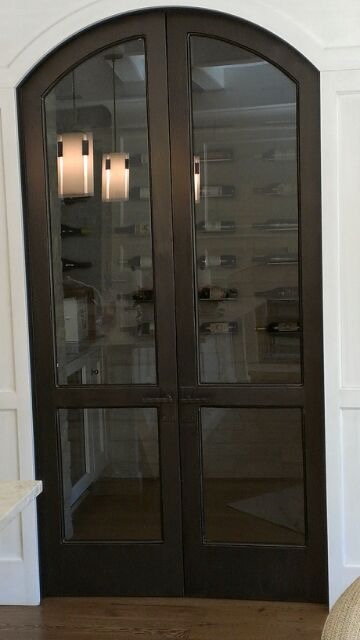 Arched steel-and-glass wine cellar doors with a warm bronze finish
